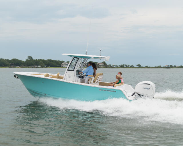 Turquoise and white center console boat running through shallow water near beach with passengers aboard