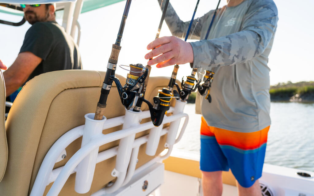 Anglers hold fishing rods mounted in rod holders on the gunwale of a bay boat