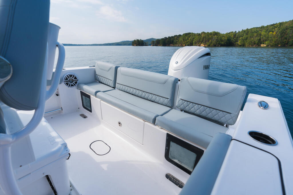 Rear seating area of center console boat with gray upholstered bench seats, Yamaha engine, and scenic lake surrounded by forested shoreline