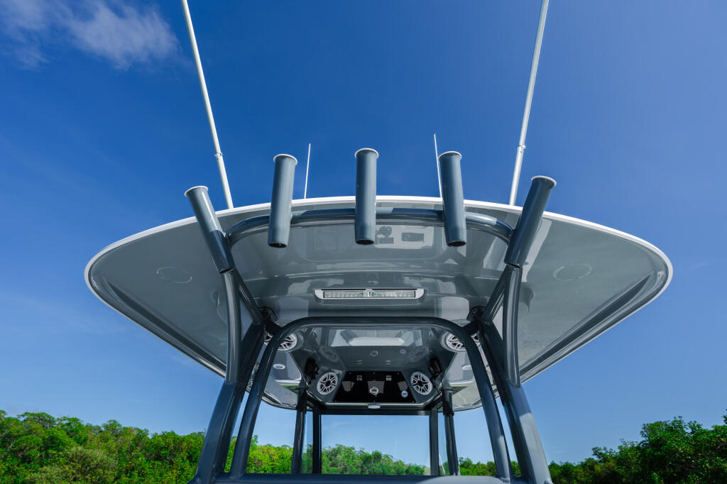Overhead view of center console boat's hard-top canopy, windshield, and helm station with antenna array against blue sky