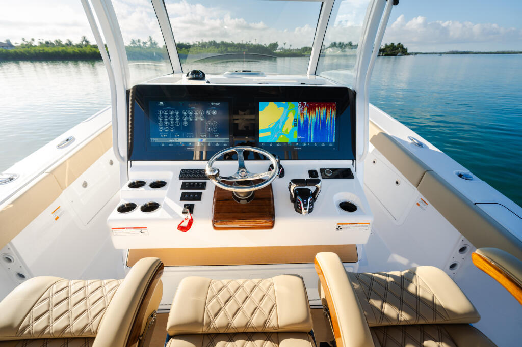 Helm station with dual displays, steering wheel, and cream-colored seating overlooking calm waters