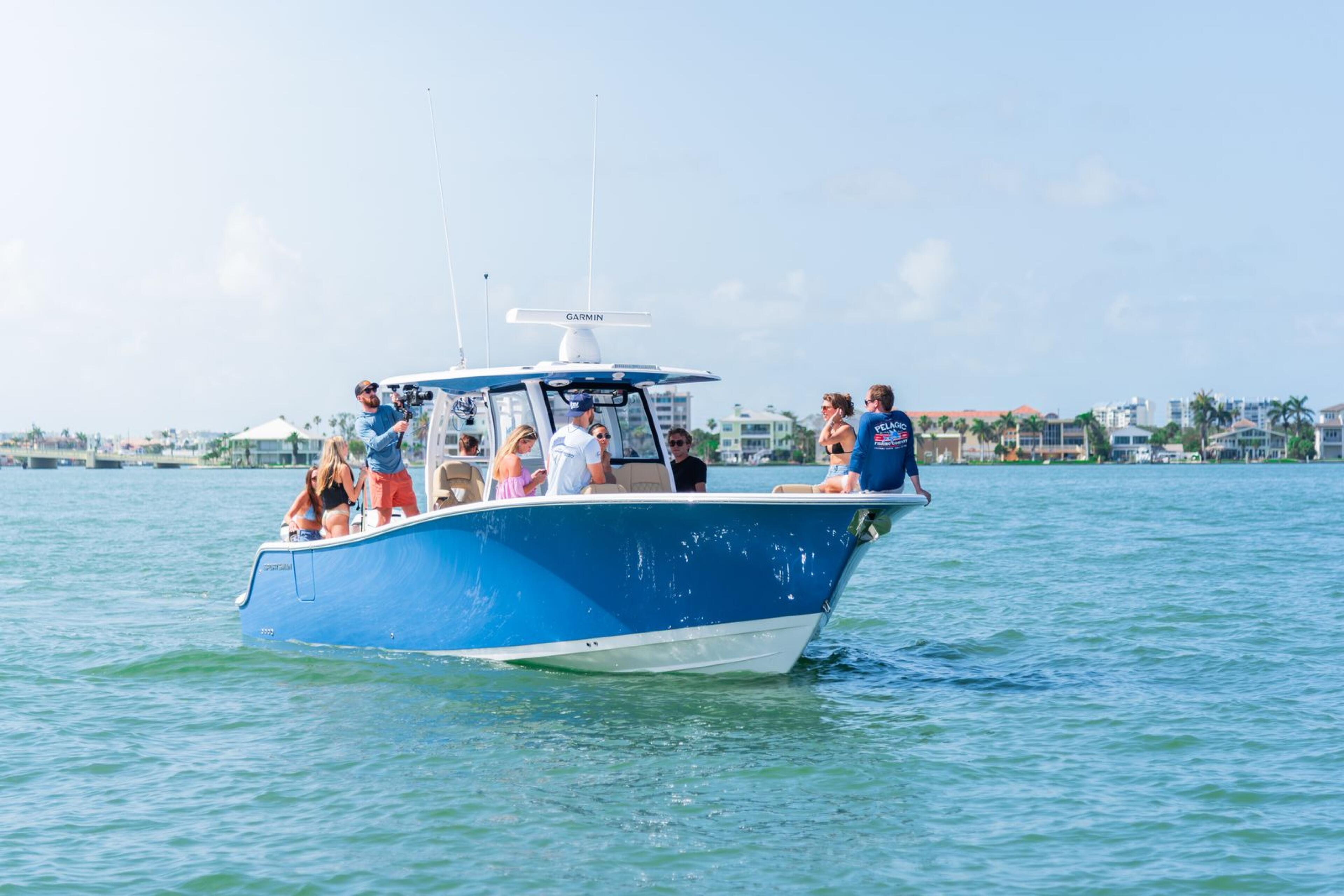 Blue and white center console boat with passengers anchored in shallow turquoise water near a palm-lined coastal town