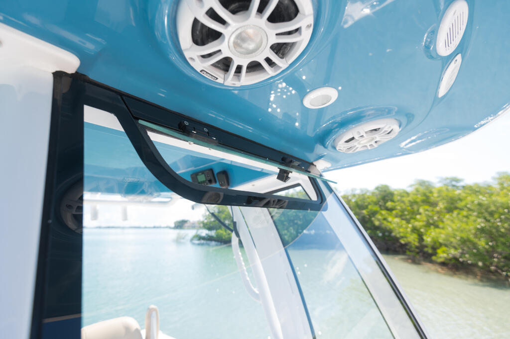 Open boat cabin with blue hardtop ceiling, speakers, vent, and tempered glass windshield overlooking coastal waters