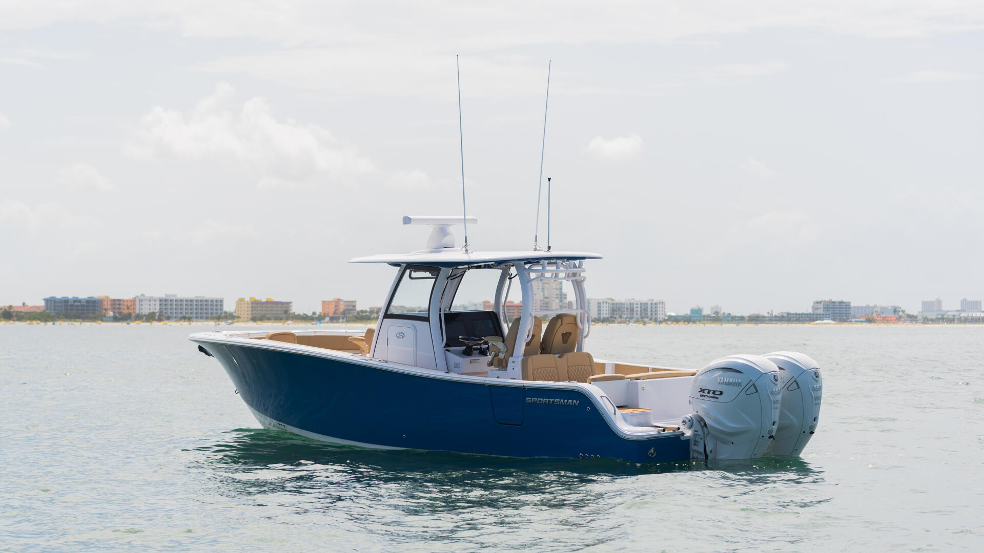 Blue and white fishing boat with dual outboard engines anchored in calm shallow water near a coastal town