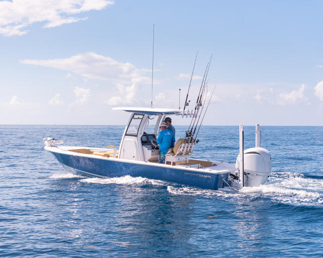 Fishing boat with multiple rod holders running through calm offshore waters in bright sunshine