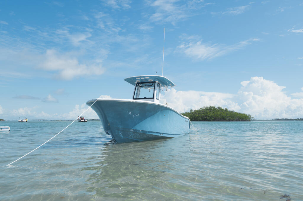 Blue center console boat moored in shallow turquoise water with mangrove island and clear sky