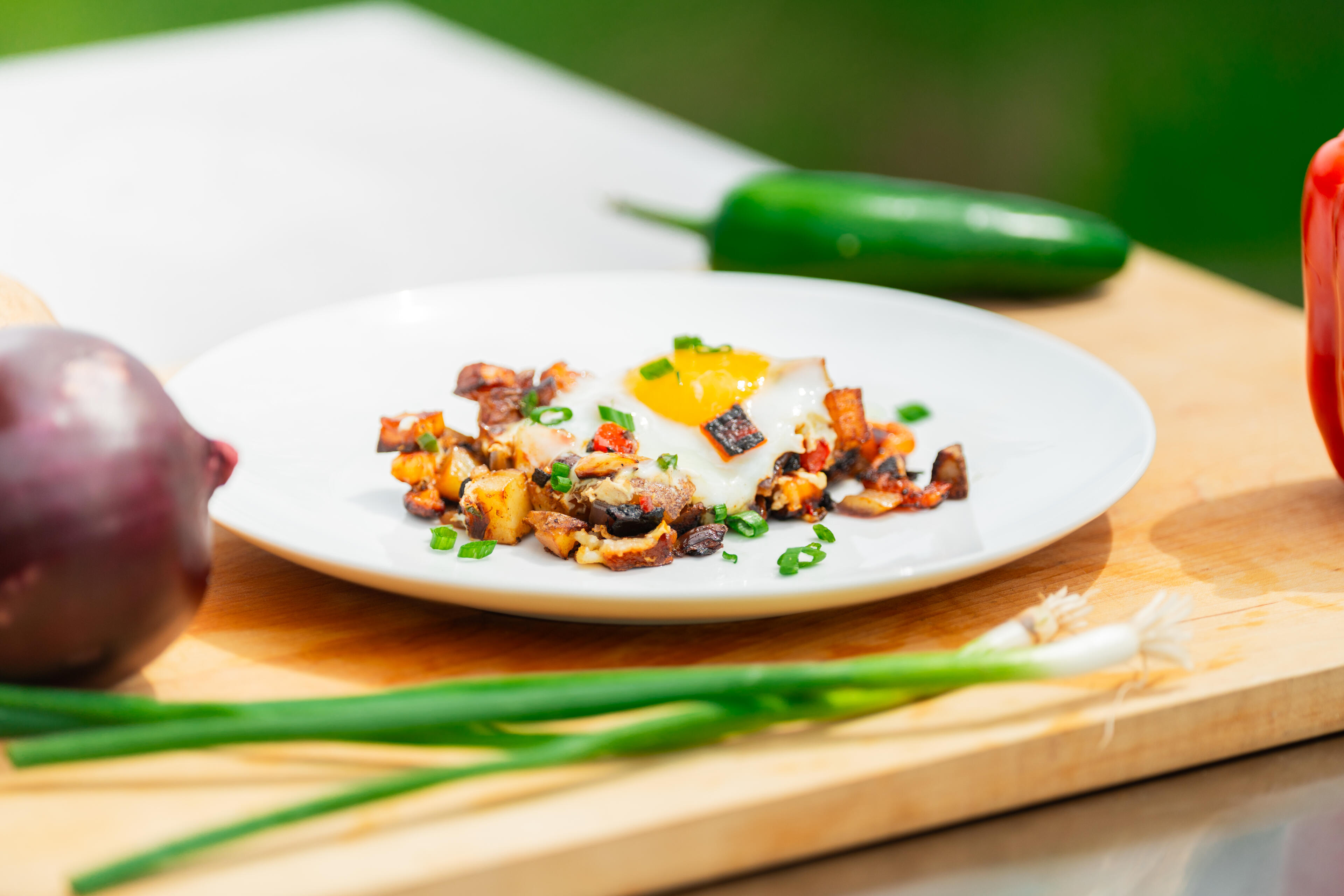 Plated lowcountry hash with crispy potatoes, egg, and green onions on white dish with fresh ingredients nearby