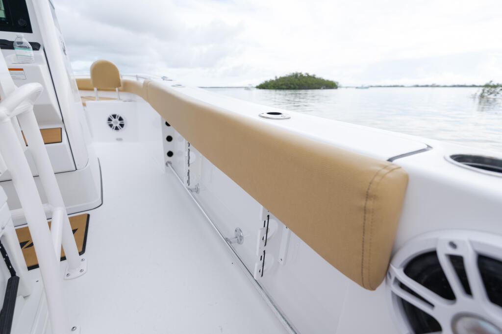 Tan bolstered seating and white gunwale of center console boat with mangrove shoreline in distance