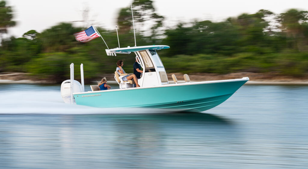 Turquoise bay boat with family cruising shallow waters near mangrove shoreline, American flag flying from hard-top