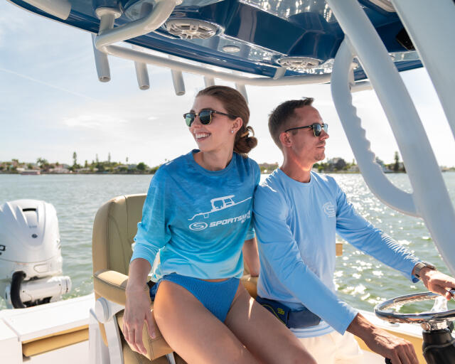 Couple enjoying a relaxing cruise at the helm of a boat with clear water and shoreline in background