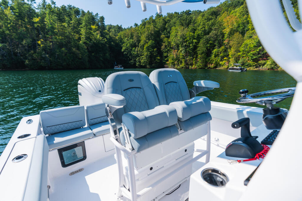 Center console boat with dual blue quilted seating and electronics on a forested lake cove
