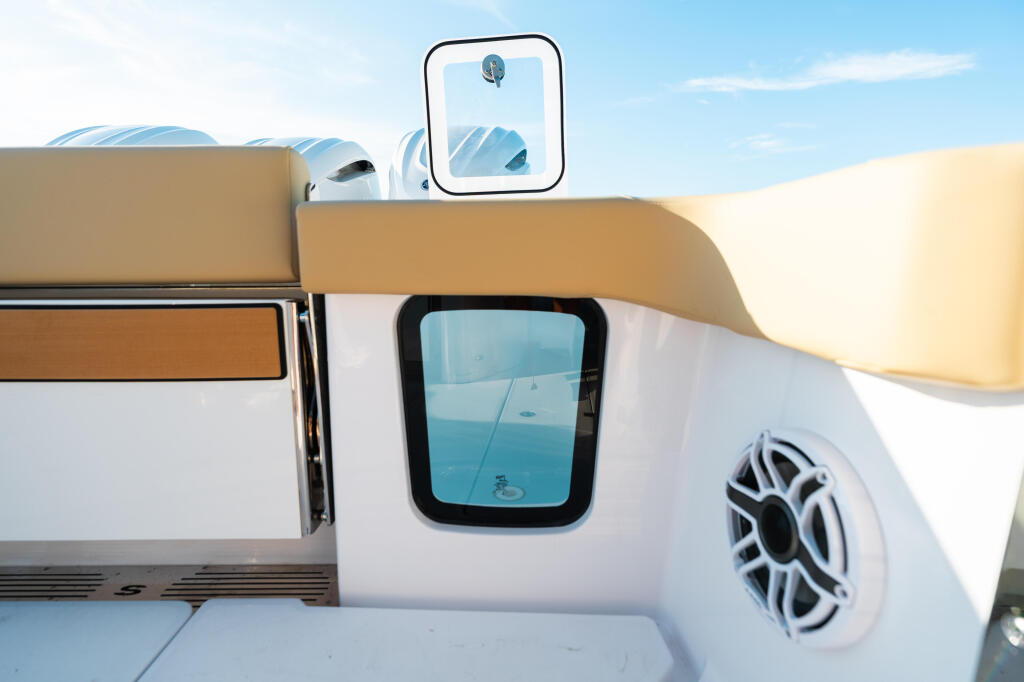 Cabin cruiser side detail showing windowed cabin, hard-top canopy, and marine audio speaker against blue sky