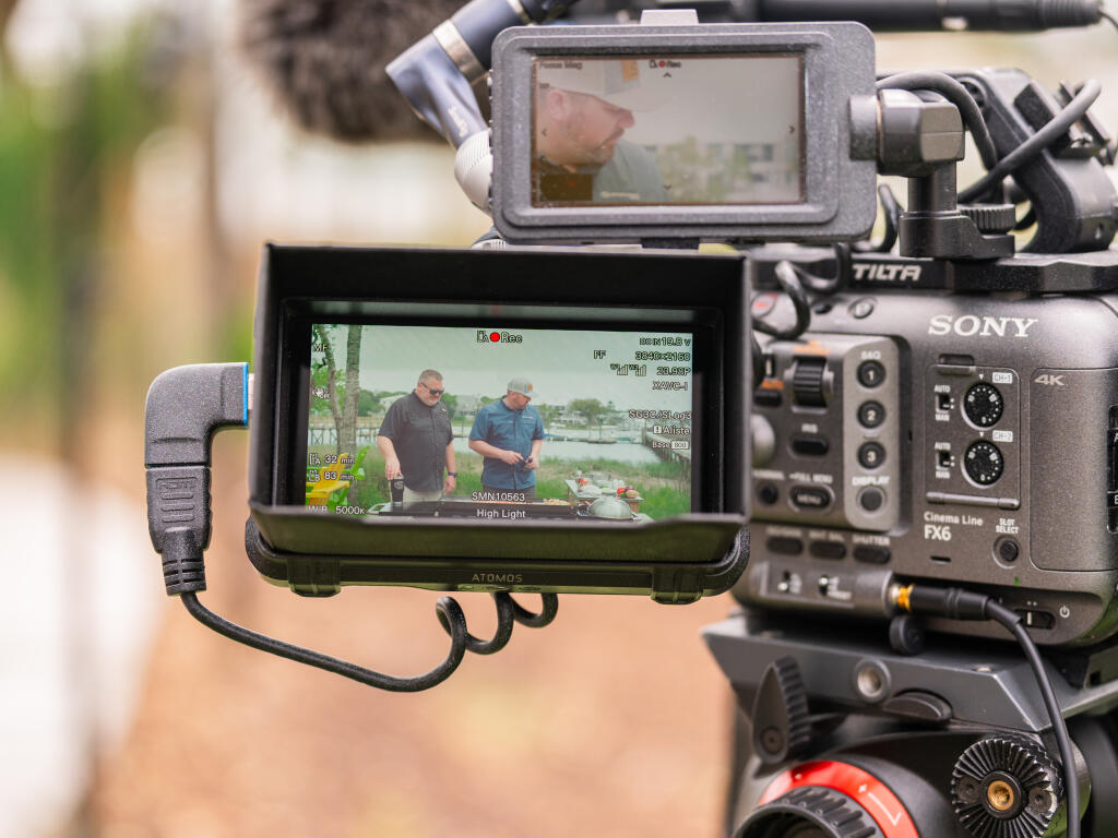 Professional video camera setup with external monitors showing two anglers fishing from a boat