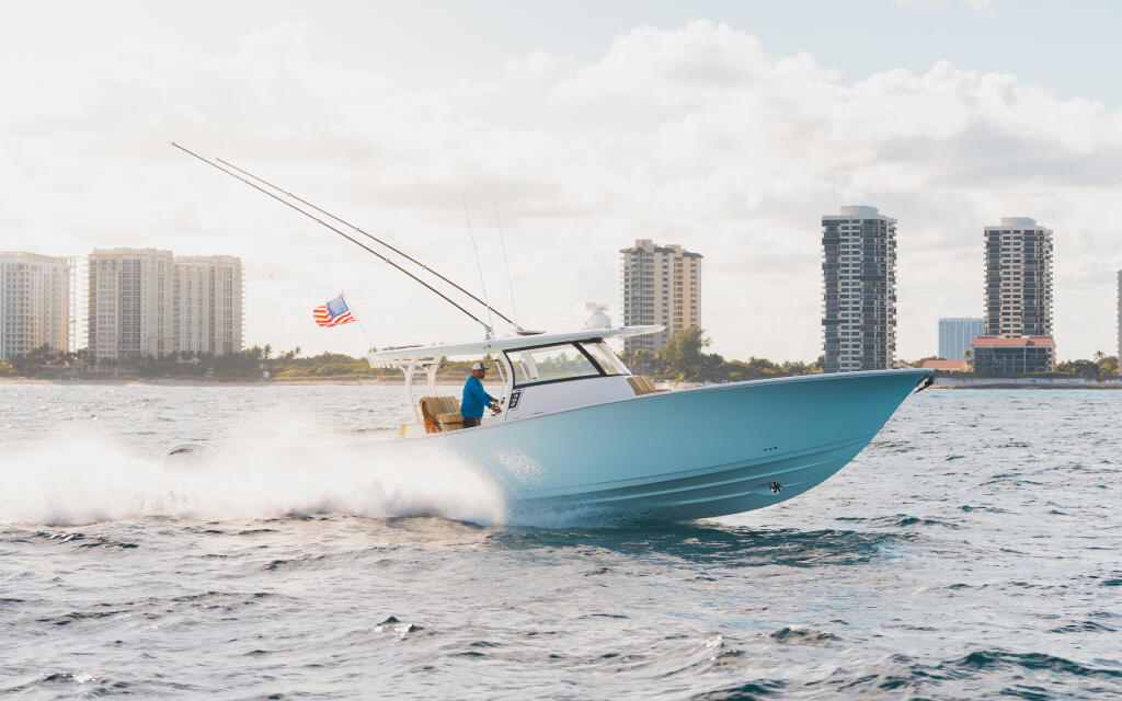 Turquoise center console boat running through beach surf with coastal high-rises in background