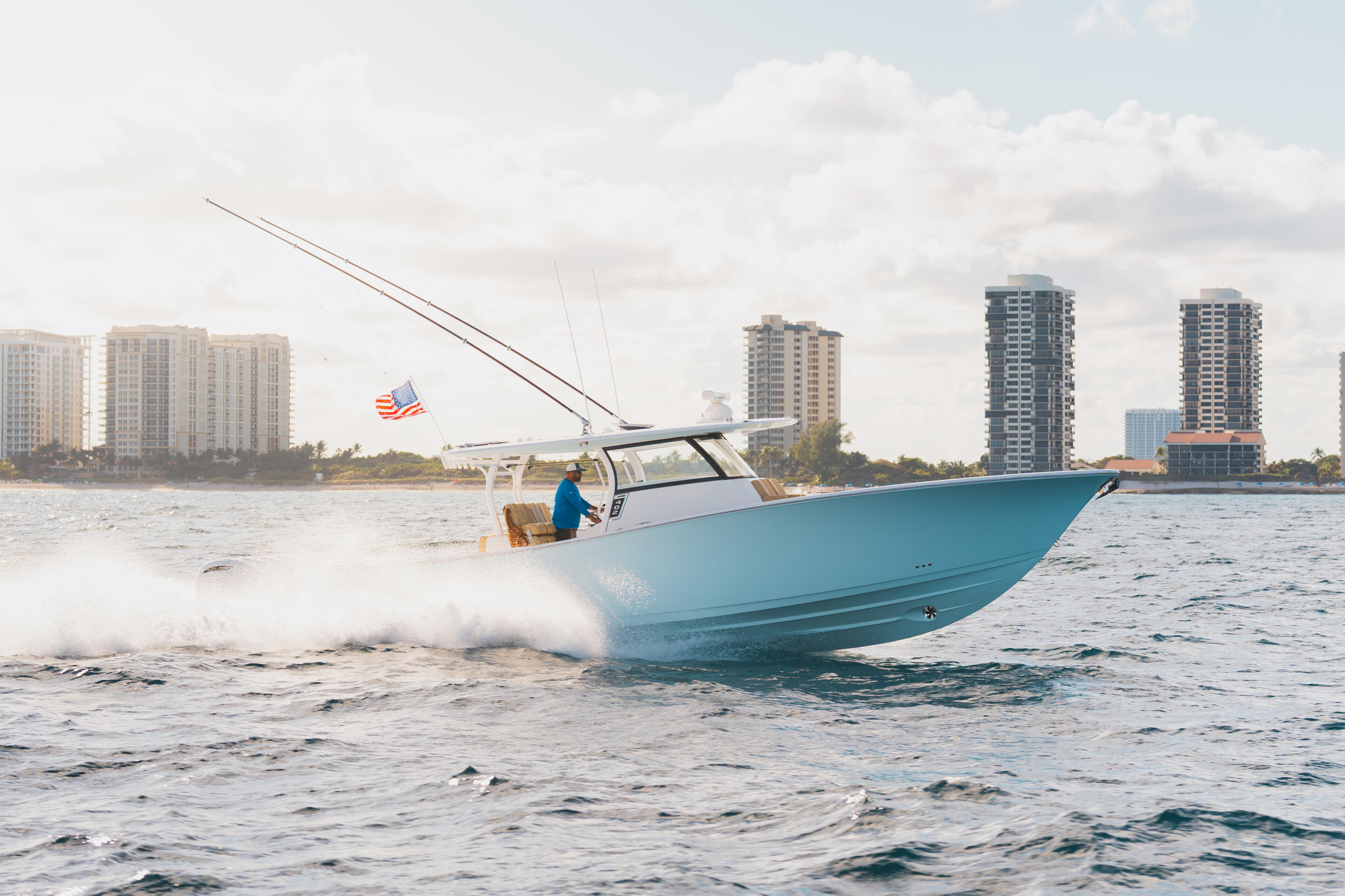 Turquoise center console boat running through beach surf with coastal high-rises in background