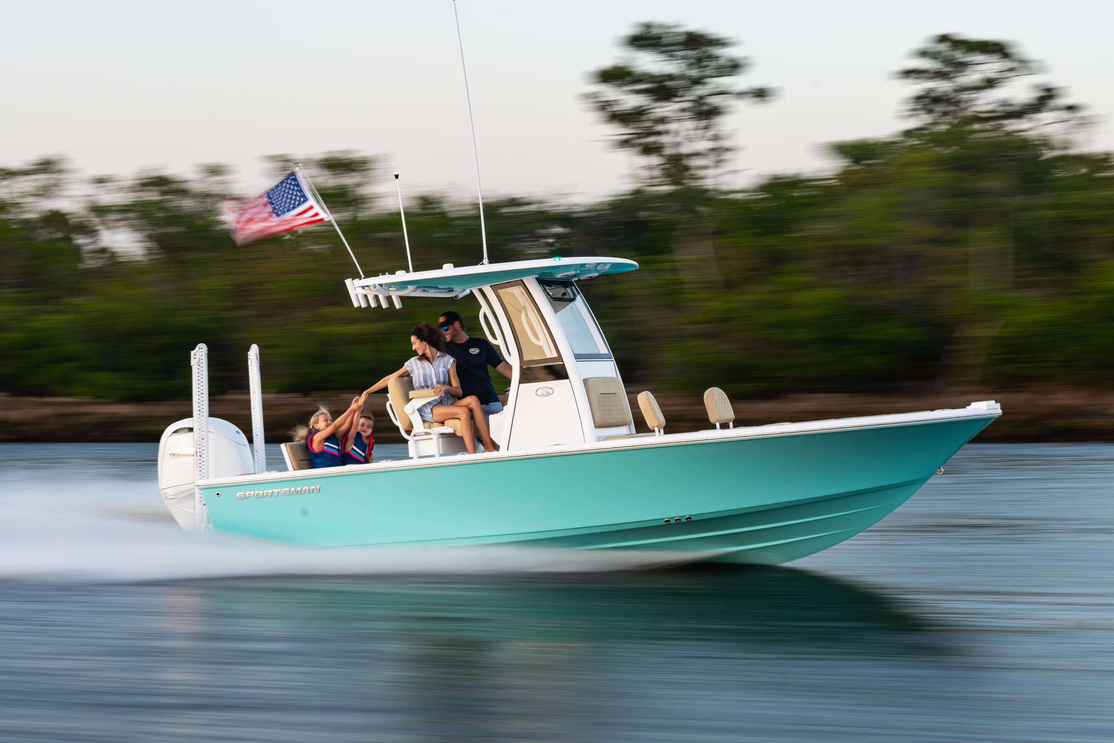 Turquoise boat with family cruising at speed, American flag flying from hardtop