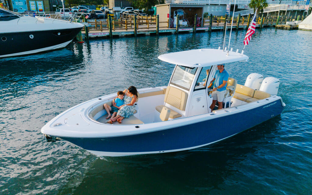 Family enjoying a blue and white center console boat at a marina with canopy top and cream seating