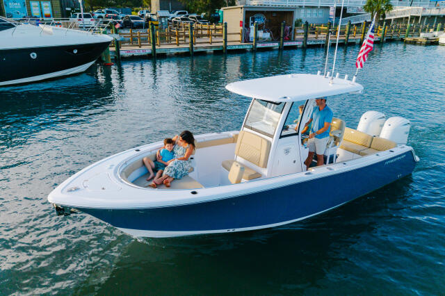 Family enjoying a blue and white center console boat at a marina with canopy top and cream seating