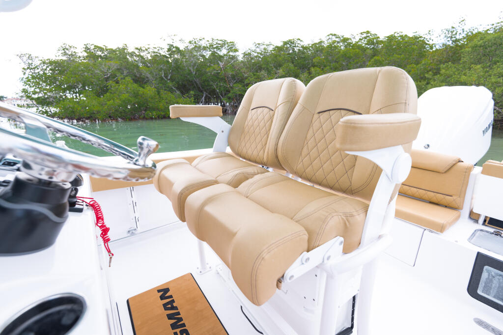 Cream leather dual captain's chairs with quilted backs and flip-up bolsters on a white center console boat near mangroves