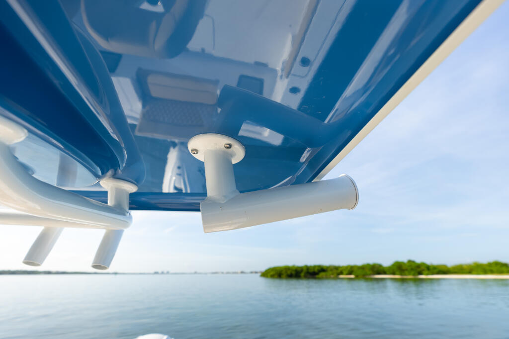 Underside view of boat's hard-top canopy with rod holders and cleats extending over calm water