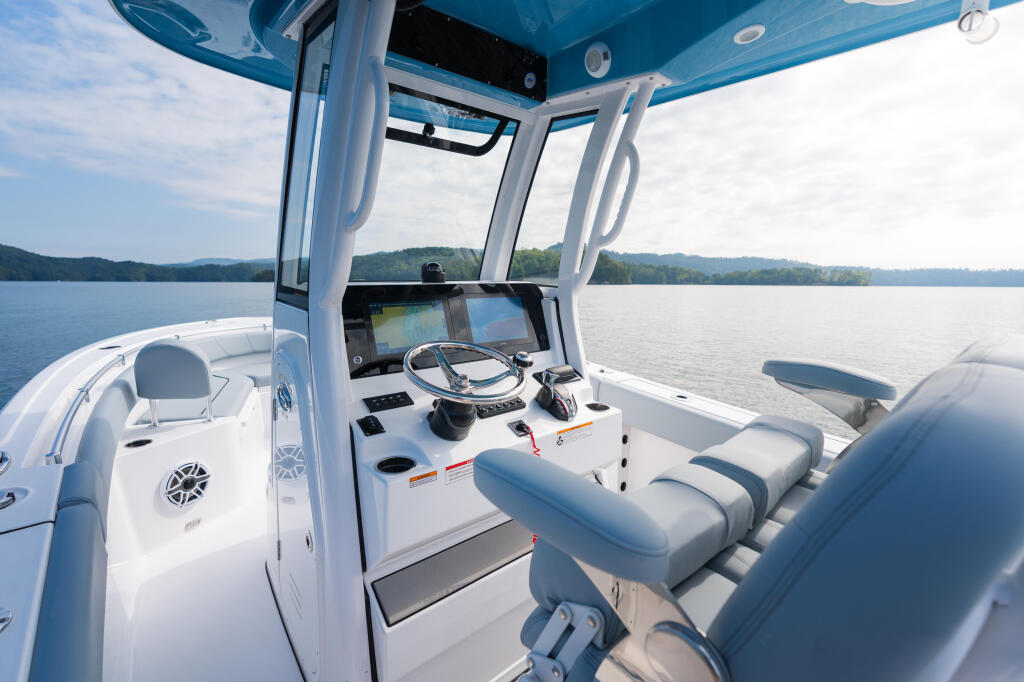 Helm station of center console boat with dual displays, steering wheel, and blue hard-top canopy overlooking calm lake