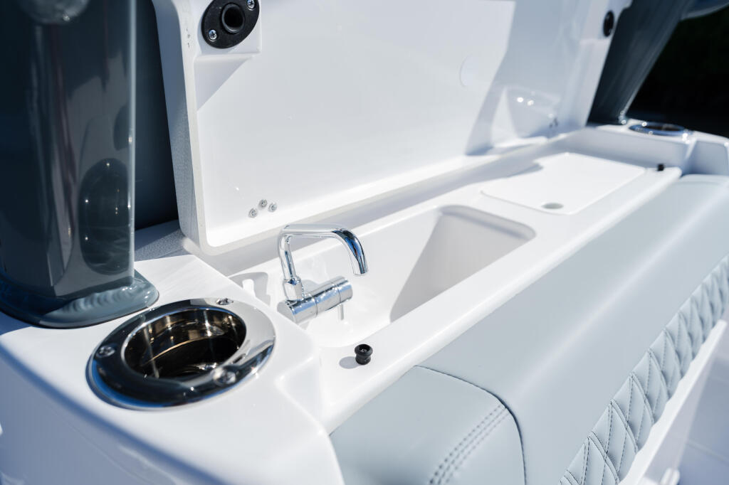 Boat console with sink, cup holder, and chrome faucet featuring white fiberglass and quilted seating