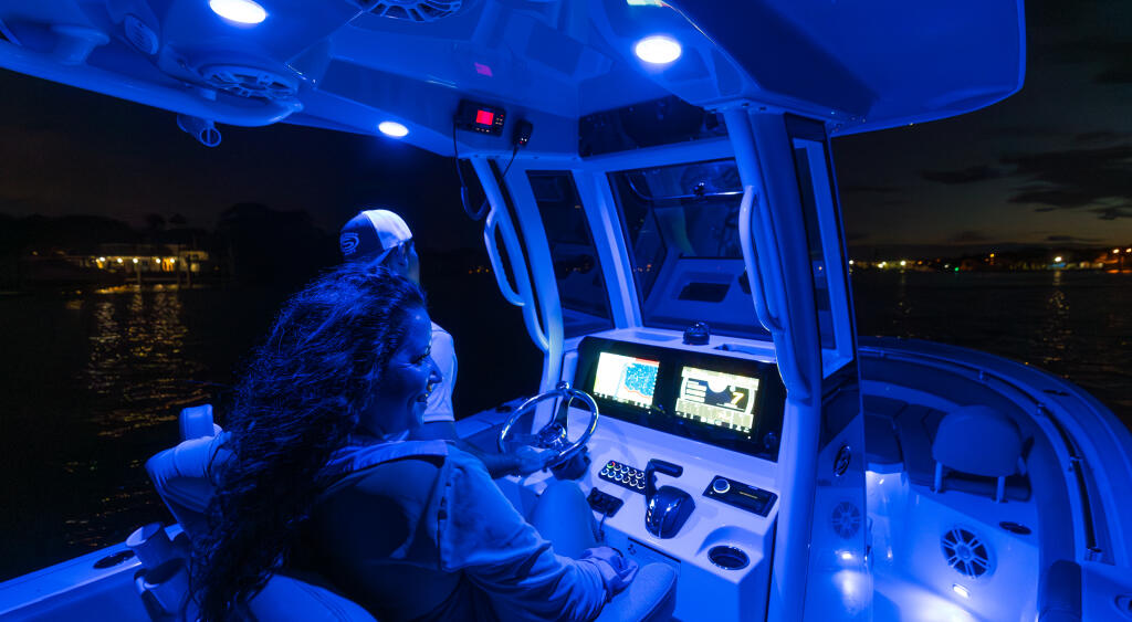 Captain at the helm of a center console boat at night with blue LED lighting and dual monitor electronics