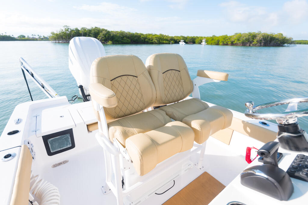 Tan leather helm seats with quilted detailing and flip-up bolsters on a white center console boat in calm blue water near mangroves