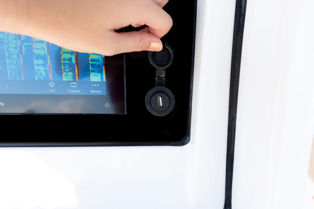 Hand holding USB headphones plugged into boat display screen showing thermal imaging sonar