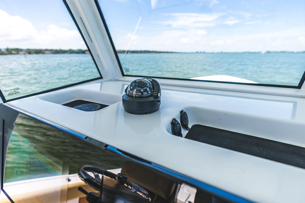 Compass mounted on helm console with windshield and turquoise bay water visible beyond