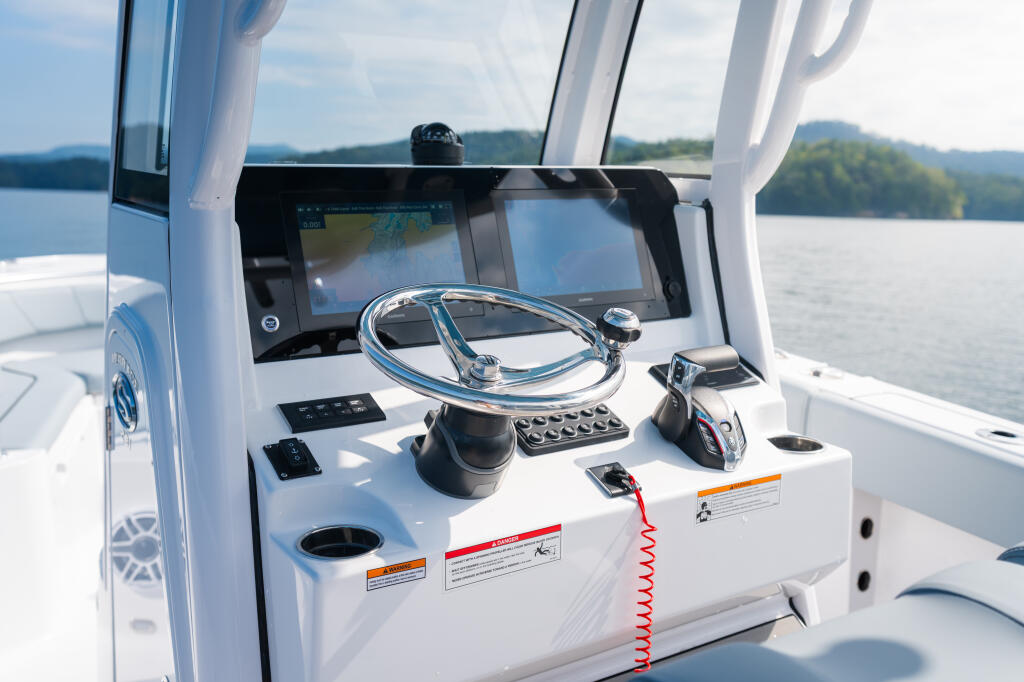 Helm station with chrome wheel, touchscreen display, and control panel overlooking calm lake with forested shoreline