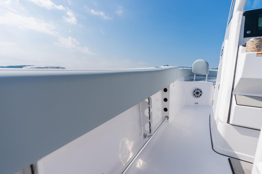 Clean white boat gunwale and deck running along calm lake with distant shoreline under blue sky