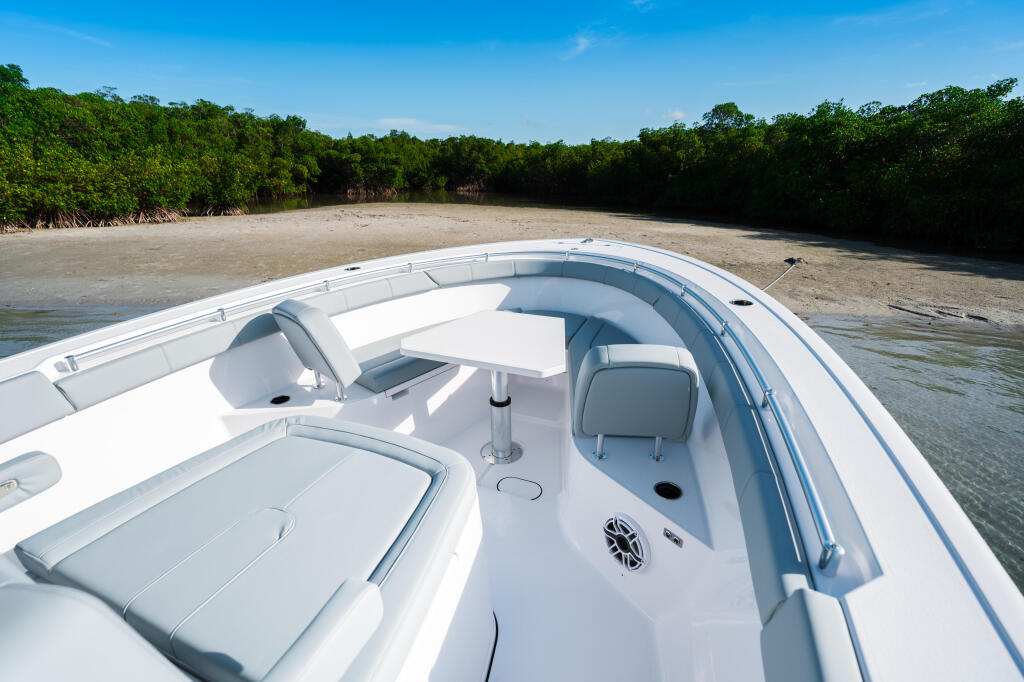 Aerial view of boat's open bow with seating, storage, and console facing a sandy beach lined with mangroves