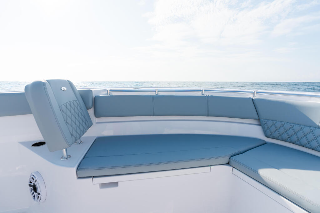 Spacious curved seating area with quilted blue upholstery and white accents overlooking calm ocean waters
