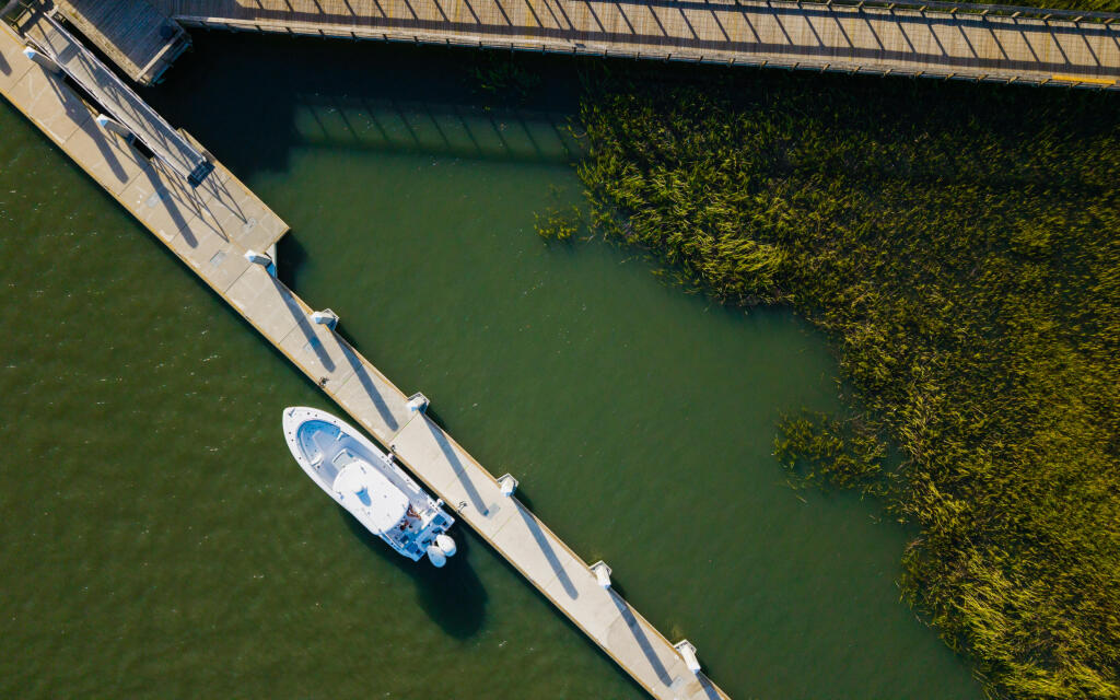 Aerial view of a white and blue boat docked at a wooden pier beside mangroves