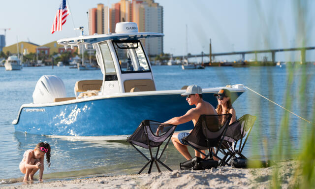 Family relaxing on a sandy beach with their blue center console boat moored nearby