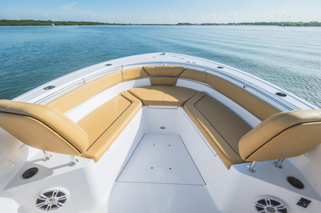 Spacious bow seating area with tan cushioned seats facing open water and tree-lined shoreline