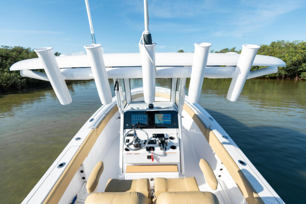 Center console boat helm with dual screens, steering wheel, and tan seating viewed from above on calm water