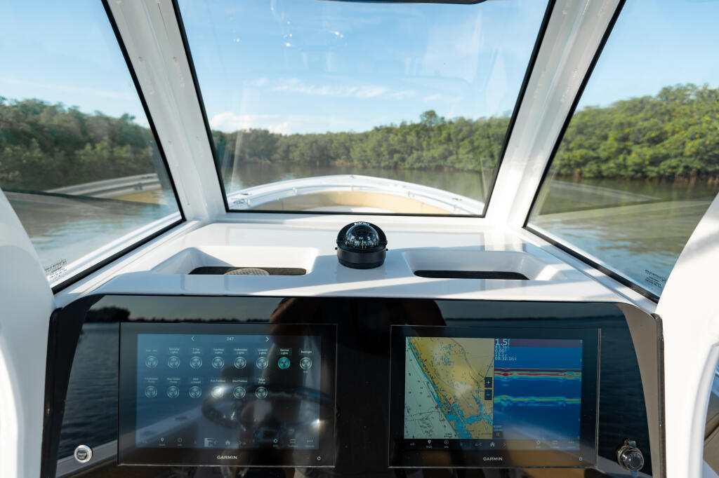 Helm station with dual Garmin displays and compass overlooking forested river channel