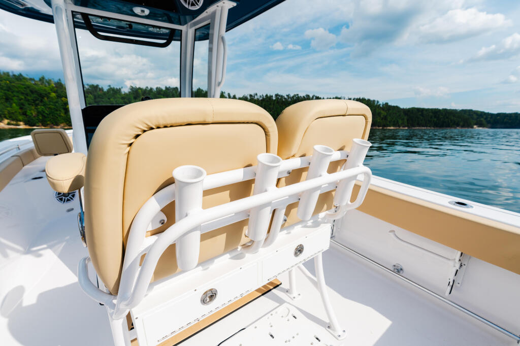 Cream-colored captain's chair and seating on a boat with white railings, positioned on calm lake waters with forested shoreline in background