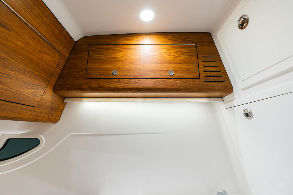 Boat cabin interior with wood cabinetry, overhead storage with dual drawers, recessed lighting, and white walls