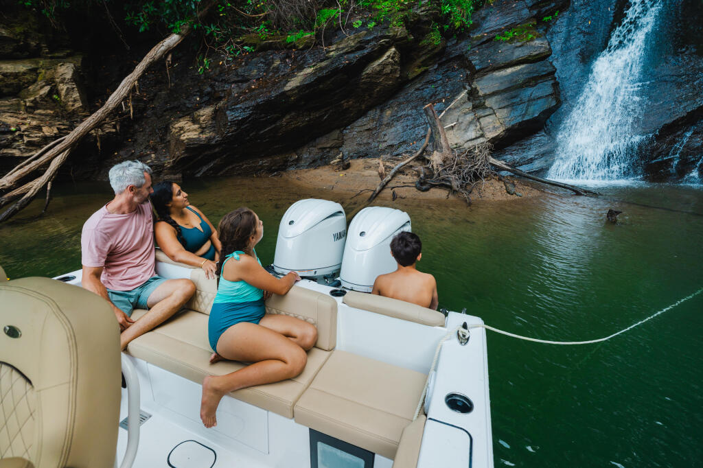 Family of four relaxes on a boat in a scenic mountain cove with waterfall