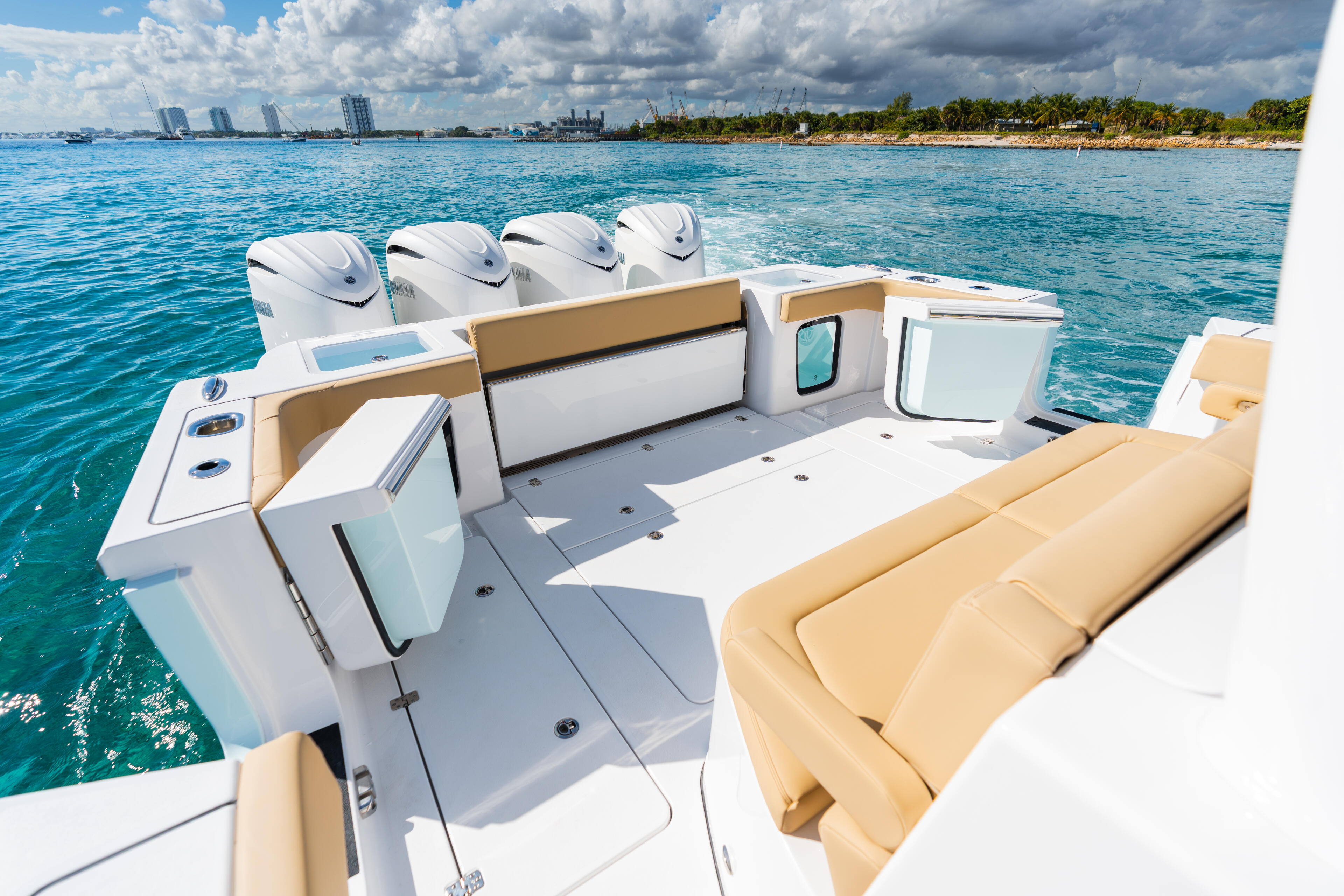 Open center console boat with tan seating and four engines anchored in turquoise water near coastal cityscape
