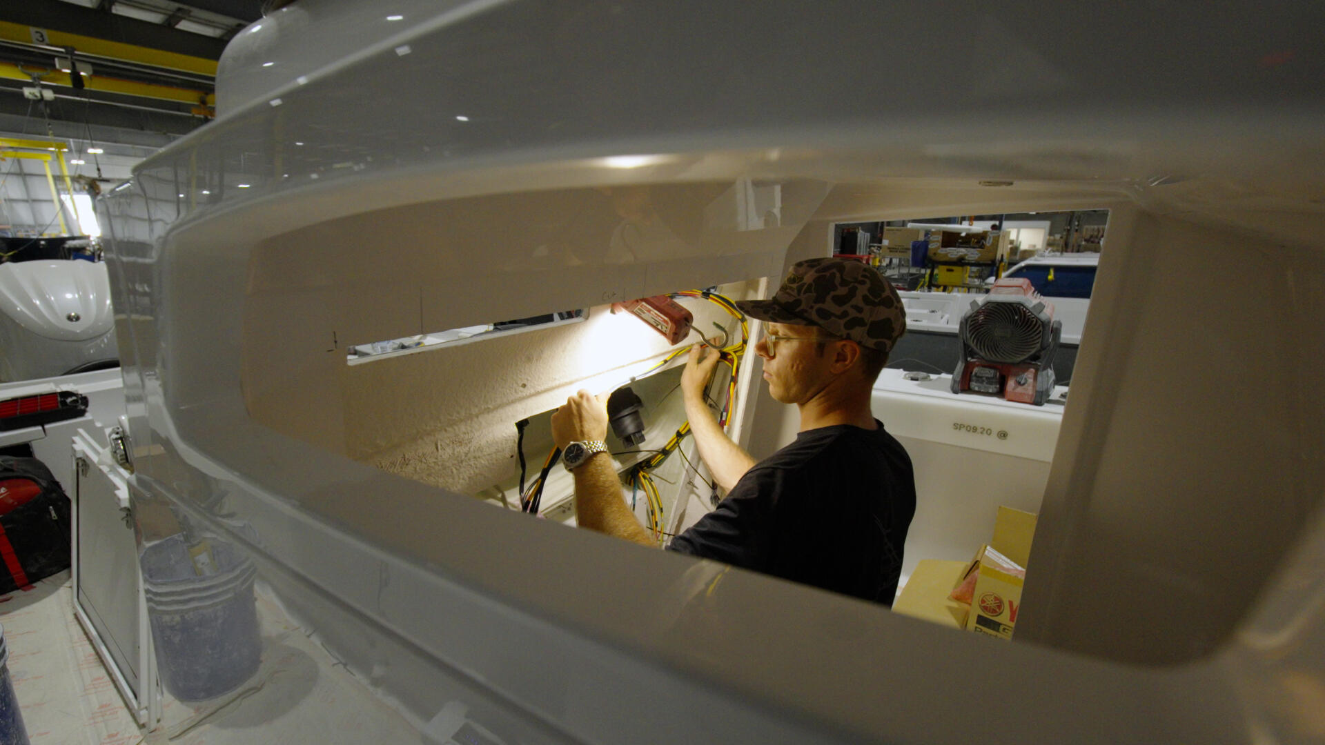 Technician installing wiring and electronics in a boat's helm console during manufacturing