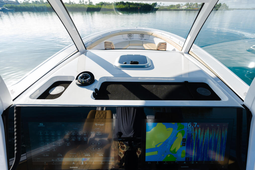 Helm station with dual Garmin displays showing navigational chart and sonar, compass, and windshield view of calm water