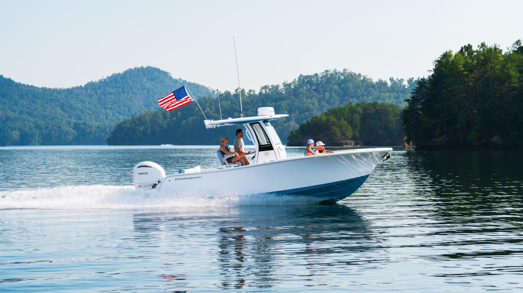 White center console boat running in shallow water near a sandbar with families aboard and mountains in background