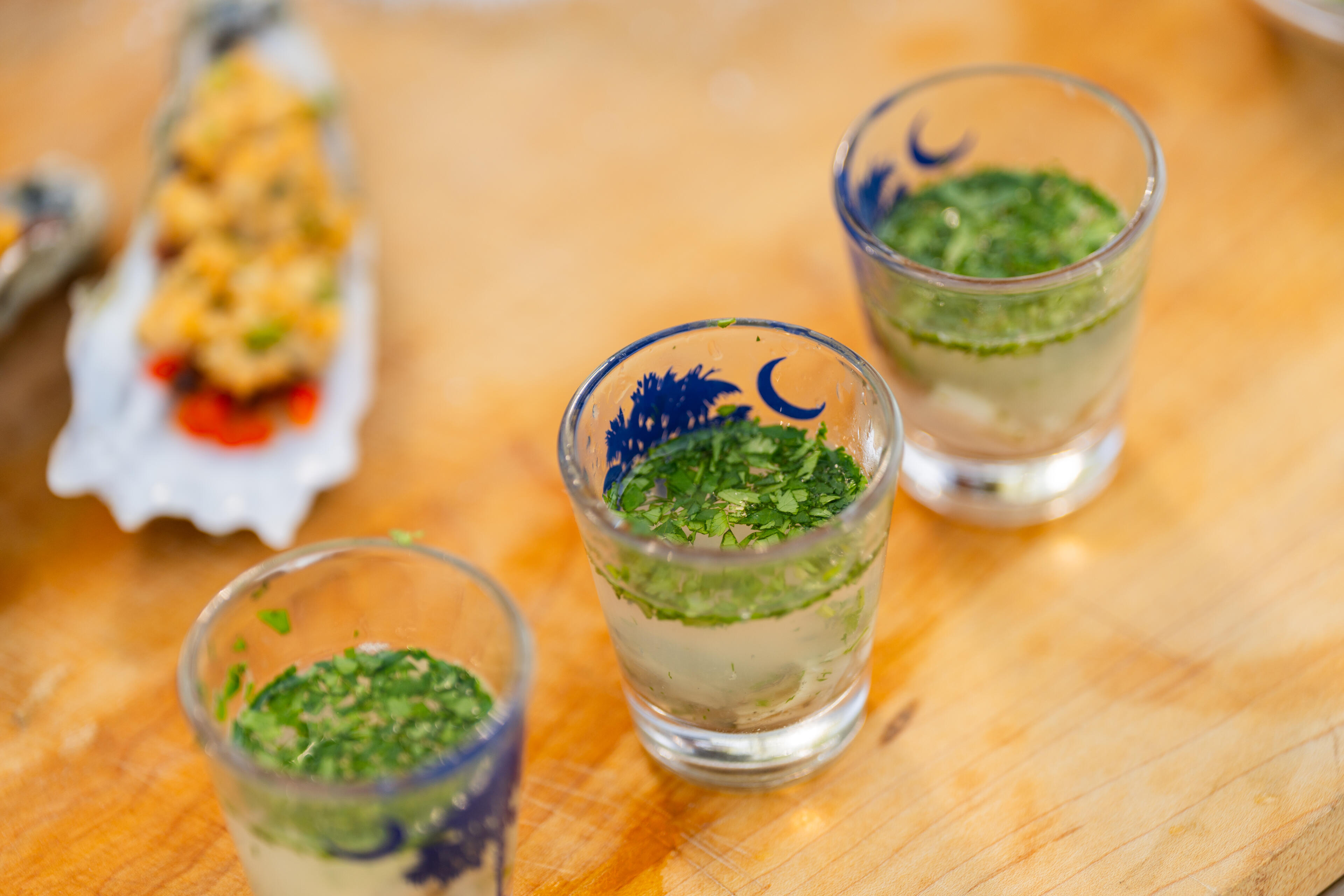 Three appetizer glasses with layered ceviche and herb garnish on a wooden surface