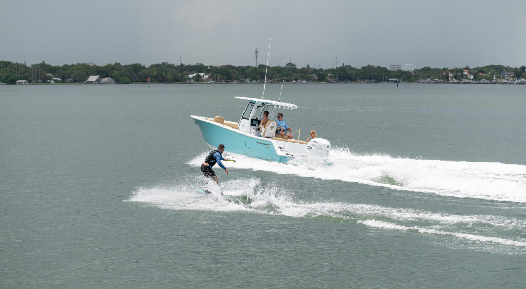 Wakeskier being towed behind a turquoise and white center console boat with passengers watching from the helm