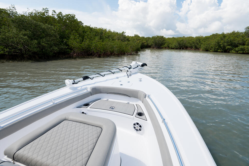 White bow seating area with quilted cushions and rod storage on a bay boat cruising past mangroves
