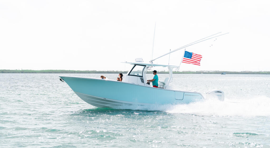 Turquoise center console boat running through shallow water with family aboard and American flag flying